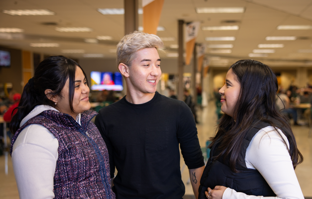 Three people engaging in a joyful conversation in a busy cafeteria setting.