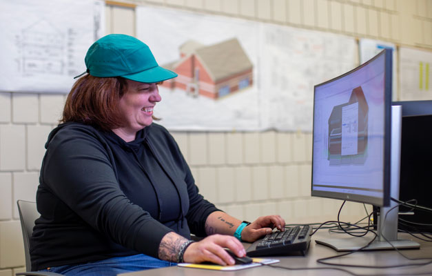 student in teal hat smiling and working in program software at computer