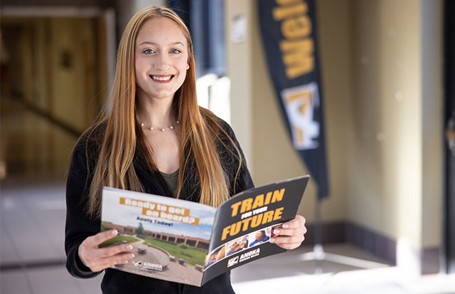 smiling student holding folder with campus photos in hallway